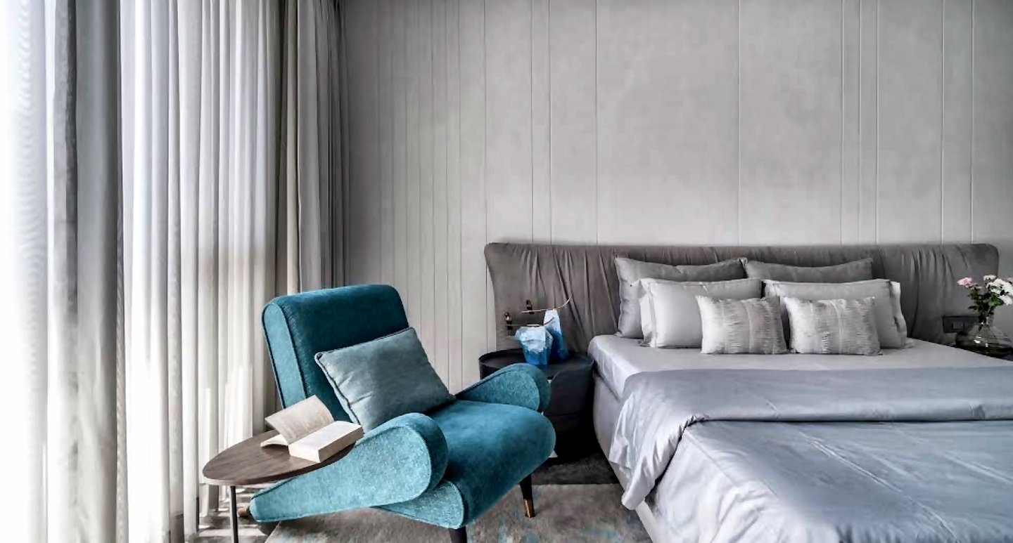 Mumbai bedroom with sheer curtains, teal accent chair and a neatly dressed mattress